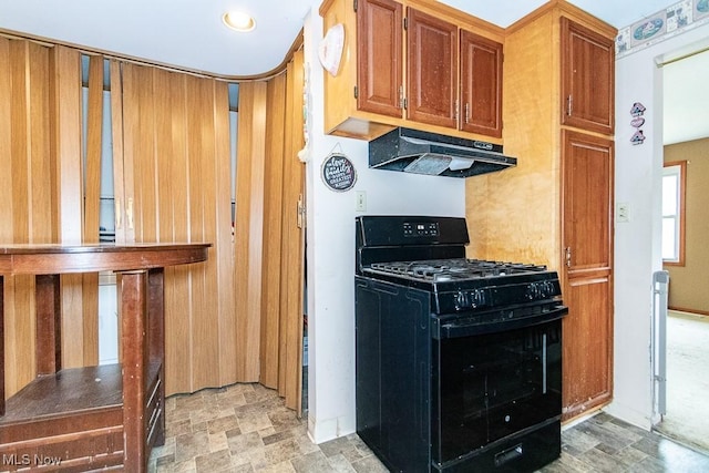 kitchen featuring black range with gas cooktop, baseboards, brown cabinetry, stone finish flooring, and under cabinet range hood