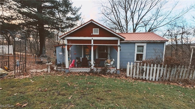 bungalow-style house featuring covered porch, metal roof, a front lawn, and fence