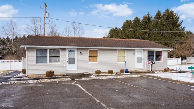 ranch-style home with uncovered parking, entry steps, roof with shingles, and fence