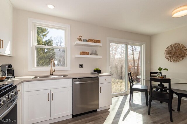 kitchen featuring stainless steel appliances, light countertops, white cabinets, a sink, and wood finished floors