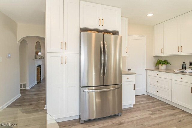 kitchen with arched walkways, visible vents, white cabinets, light wood-type flooring, and freestanding refrigerator