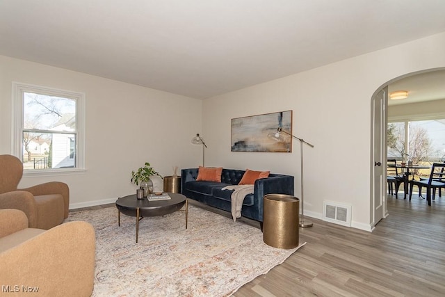 living room featuring arched walkways, visible vents, baseboards, and wood finished floors