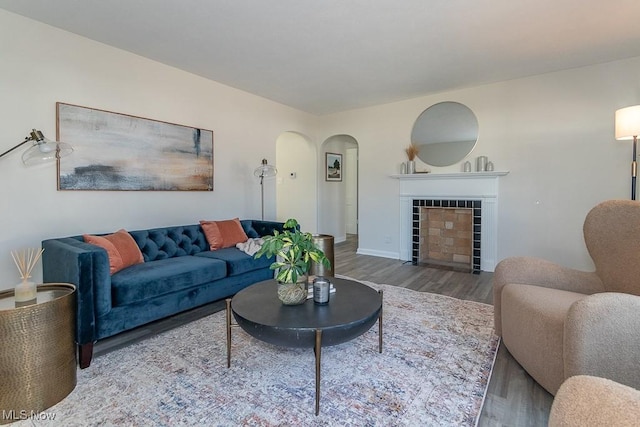 living area featuring baseboards, a fireplace, arched walkways, and wood finished floors