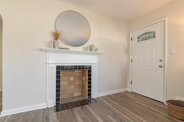 foyer entrance with wood finished floors, a tile fireplace, and baseboards