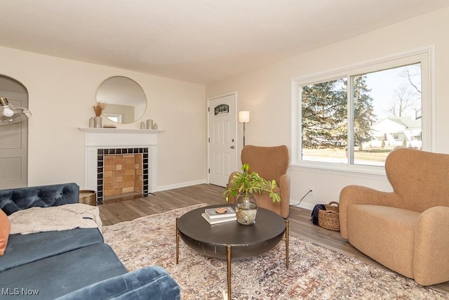 living room featuring a tile fireplace, baseboards, and wood finished floors