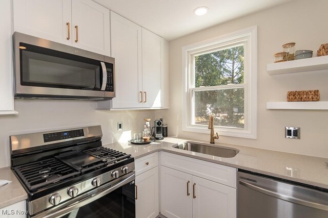 kitchen featuring open shelves, appliances with stainless steel finishes, a sink, and white cabinetry