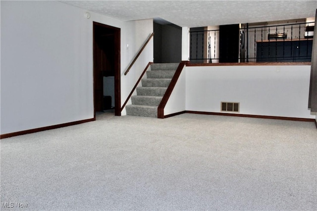 carpeted empty room with a textured ceiling, stairs, visible vents, and baseboards