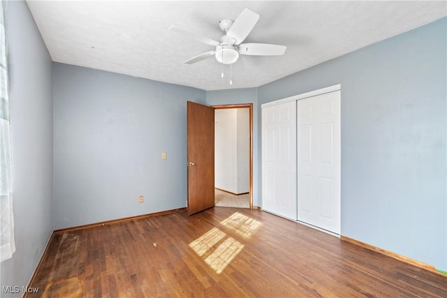 unfurnished bedroom featuring ceiling fan, a closet, baseboards, and wood finished floors