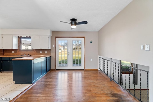 kitchen with tasteful backsplash, white cabinets, a sink, light wood-type flooring, and a peninsula