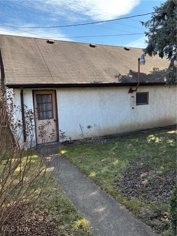 view of exterior entry featuring a yard, roof with shingles, and stucco siding