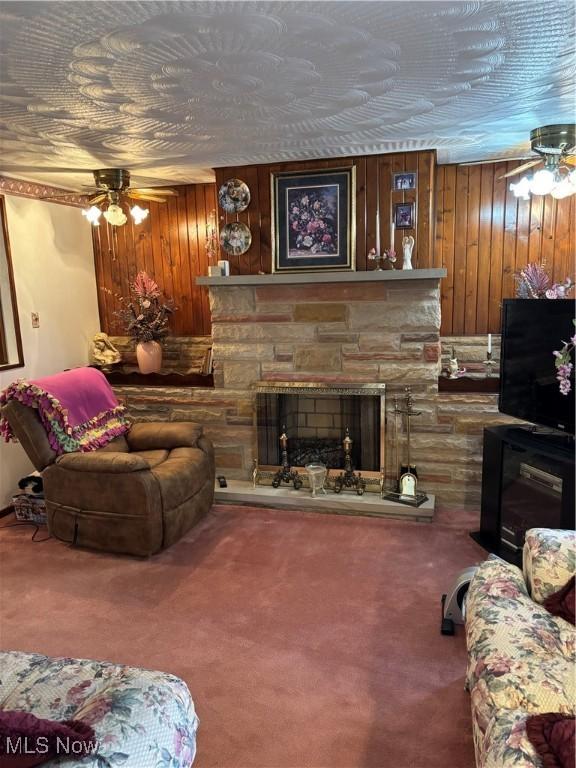 living room featuring a ceiling fan, carpet, and a stone fireplace