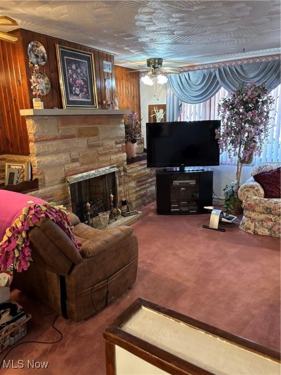 living area with a ceiling fan, carpet flooring, and a stone fireplace