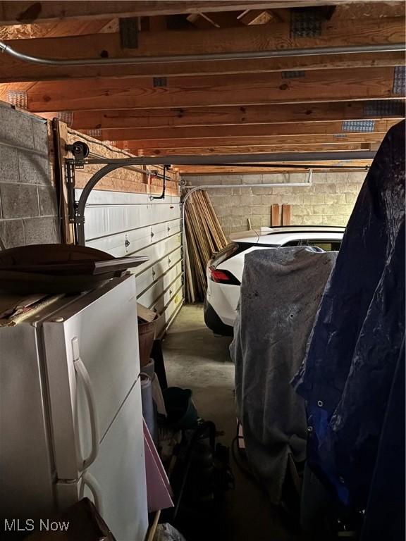 interior space with a garage, wood walls, freestanding refrigerator, and concrete block wall