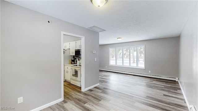 spare room featuring light wood finished floors, baseboard heating, and baseboards