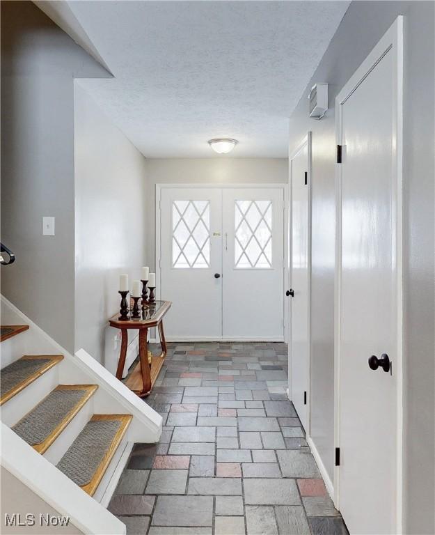 foyer entrance featuring french doors, stone finish flooring, stairway, and a textured ceiling