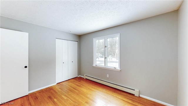 unfurnished bedroom with baseboards, a baseboard radiator, light wood-style flooring, a textured ceiling, and a closet