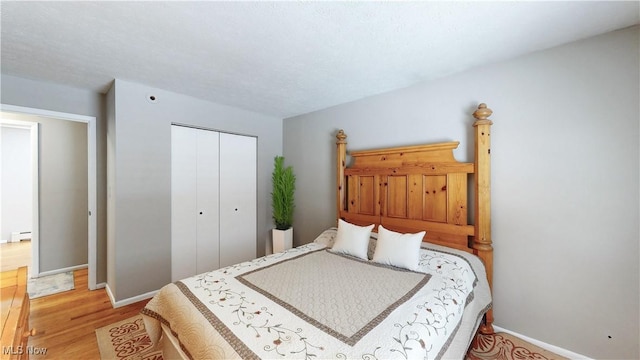 bedroom with light wood-type flooring, a closet, baseboards, and baseboard heating