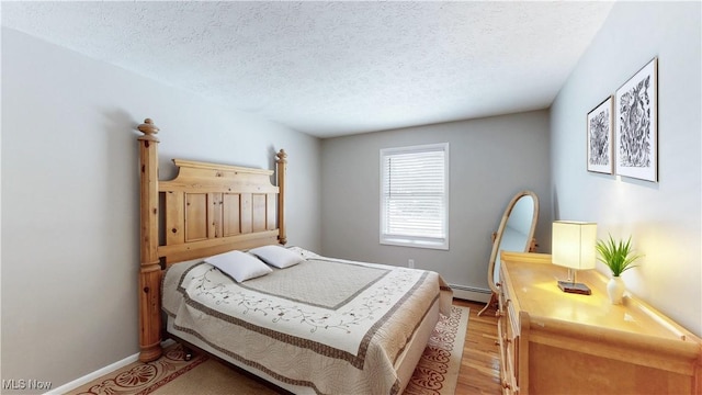 bedroom with light wood-type flooring, baseboards, baseboard heating, and a textured ceiling