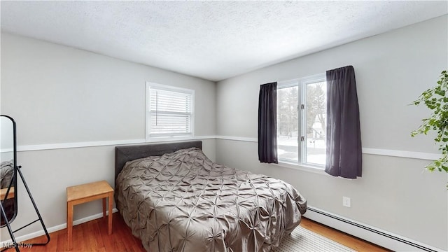 bedroom with a textured ceiling, a baseboard radiator, multiple windows, and wood finished floors