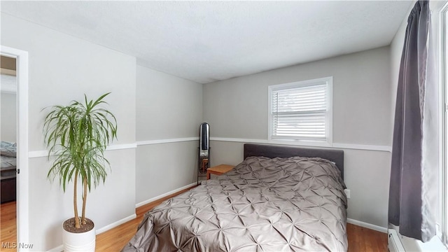 bedroom with baseboards, a baseboard heating unit, and wood finished floors