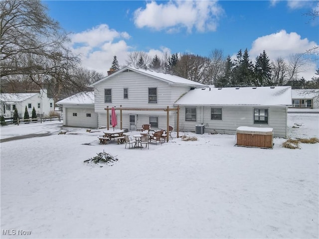 snow covered house with a garage, cooling unit, an outdoor fire pit, and a hot tub