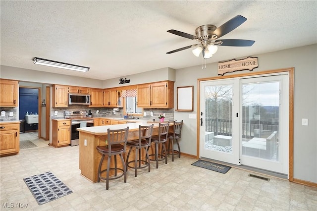 kitchen with light floors, stainless steel appliances, light countertops, a sink, and a kitchen bar