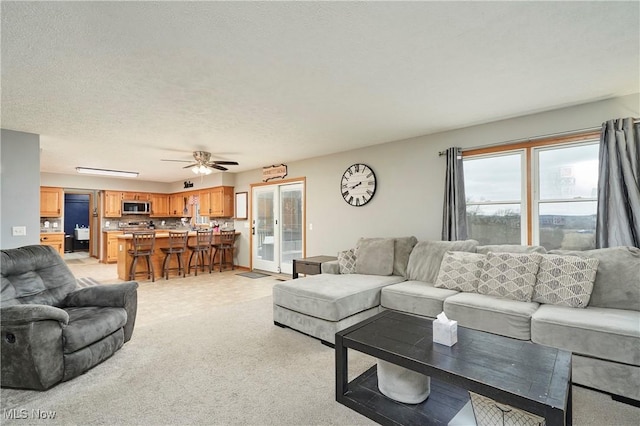 living area with a ceiling fan, a textured ceiling, and light colored carpet