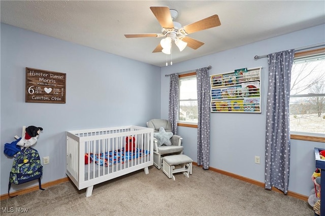 bedroom with carpet floors, a nursery area, baseboards, and a ceiling fan