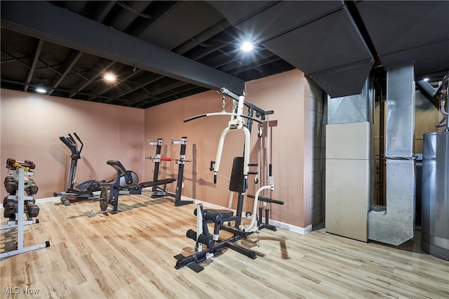 exercise room with baseboards, water heater, heating unit, and wood finished floors