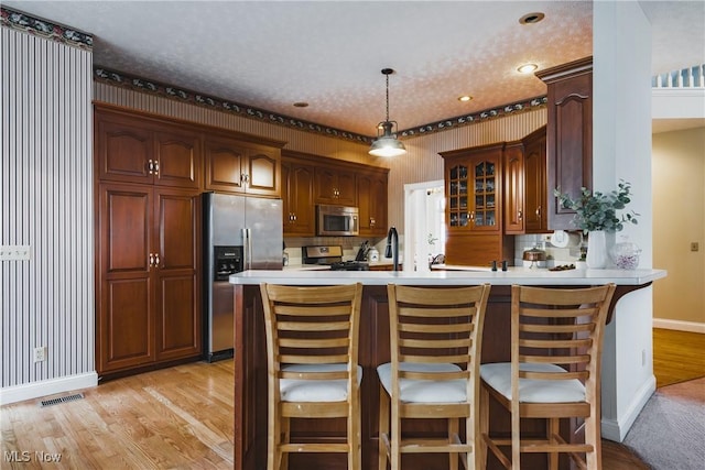 kitchen with visible vents, appliances with stainless steel finishes, glass insert cabinets, a peninsula, and wallpapered walls