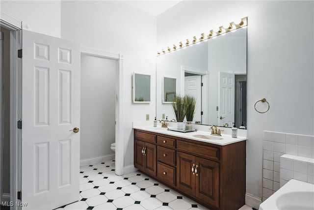 bathroom featuring a bath, a sink, toilet, and double vanity