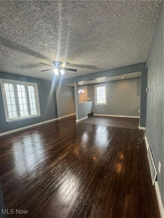 unfurnished living room featuring a textured ceiling, a ceiling fan, visible vents, baseboards, and wood-type flooring