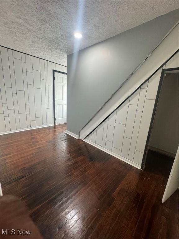 unfurnished living room featuring a textured ceiling, baseboards, and wood finished floors