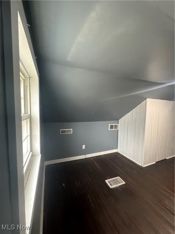 additional living space featuring baseboards, vaulted ceiling, visible vents, and dark wood finished floors