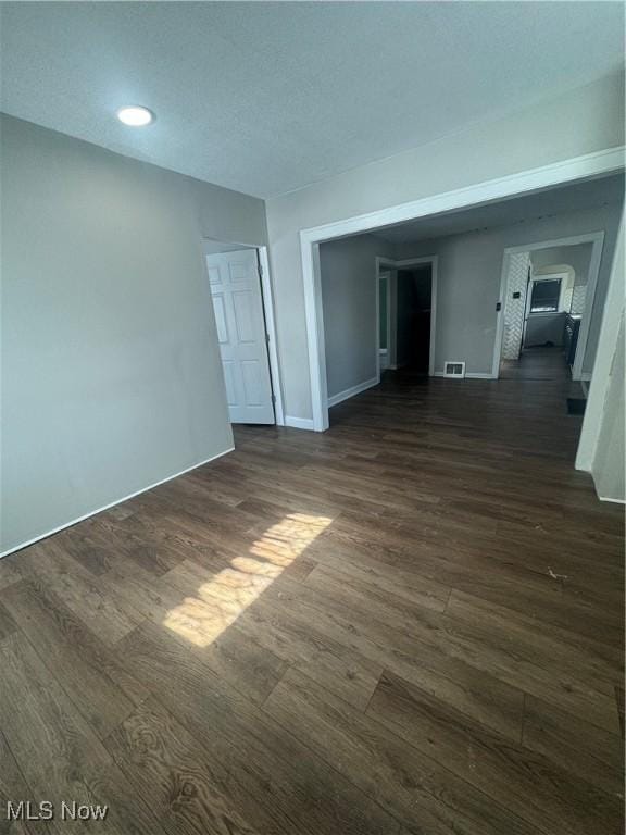 unfurnished room with dark wood-type flooring, visible vents, and baseboards