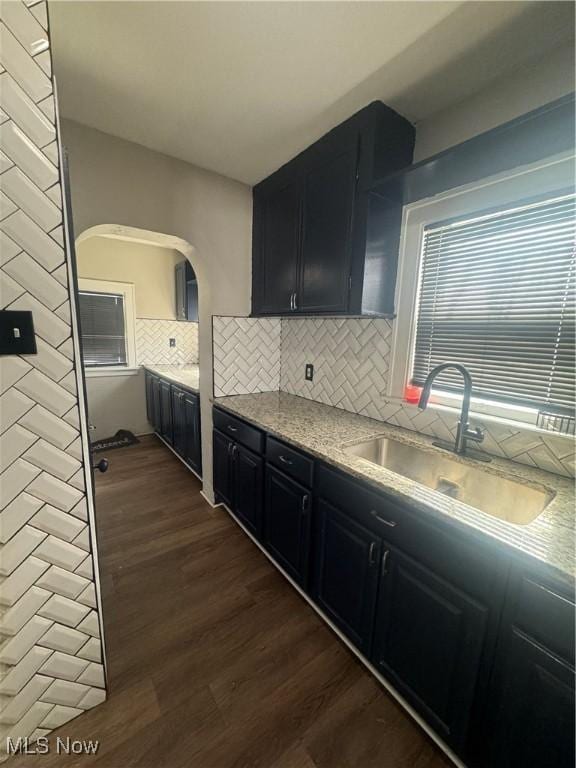 kitchen featuring dark wood finished floors, tasteful backsplash, a sink, light stone countertops, and dark cabinetry