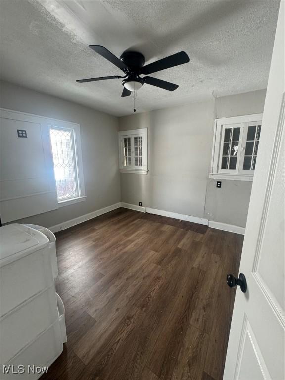 unfurnished room featuring dark wood-type flooring, a textured ceiling, and baseboards