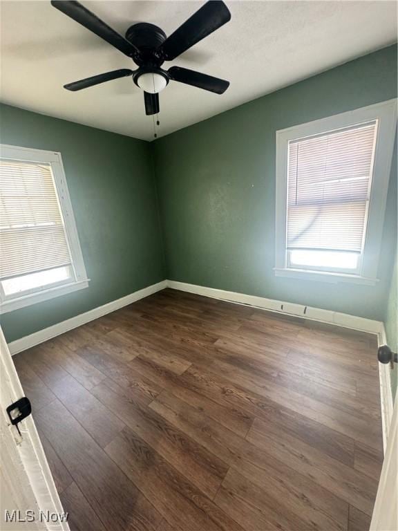 spare room featuring a healthy amount of sunlight, a ceiling fan, baseboards, and dark wood-type flooring