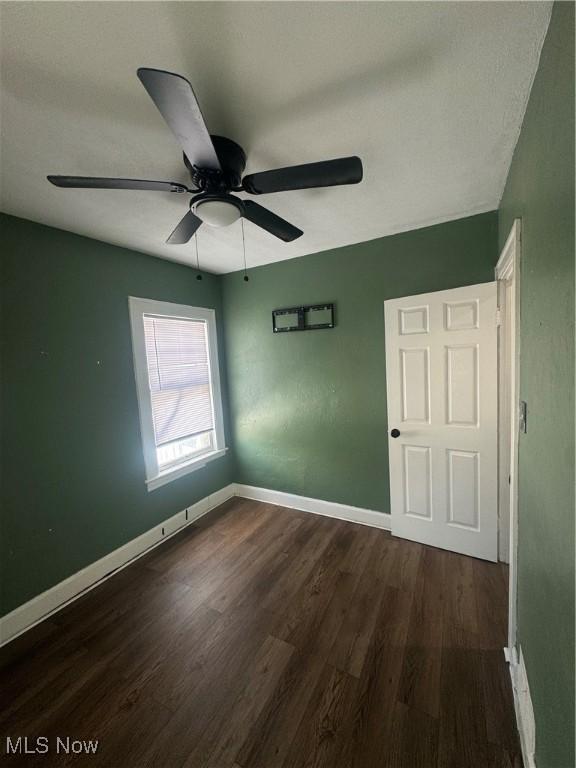 unfurnished bedroom featuring dark wood-style floors, baseboards, and a ceiling fan