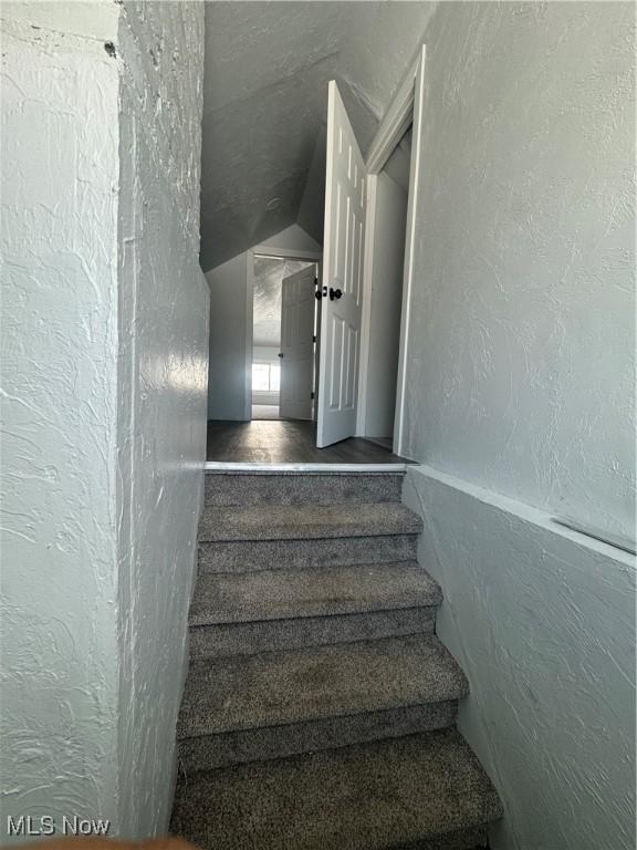 stairway featuring vaulted ceiling and a textured wall