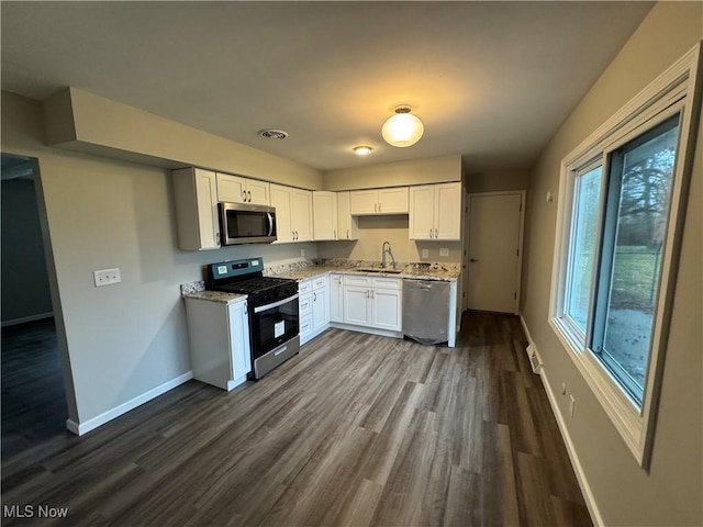 kitchen featuring dark wood-style flooring, a sink, white cabinets, baseboards, and appliances with stainless steel finishes