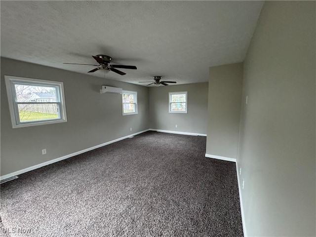 empty room with a wall unit AC, baseboards, dark carpet, and a textured ceiling