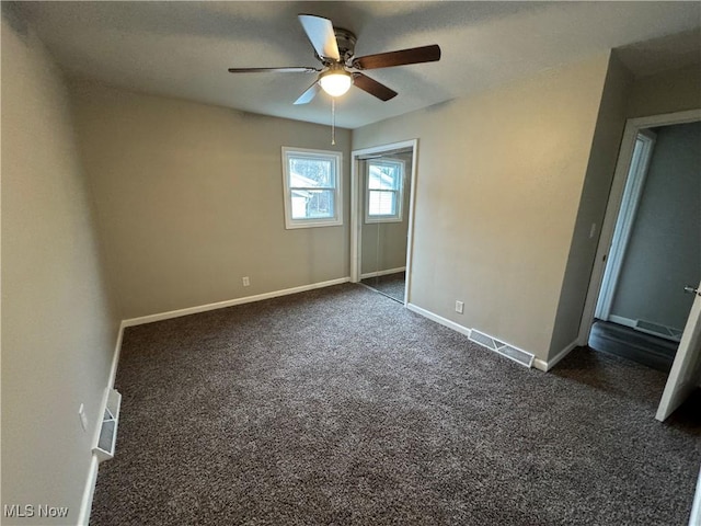 unfurnished bedroom with baseboards, visible vents, dark carpet, and a ceiling fan