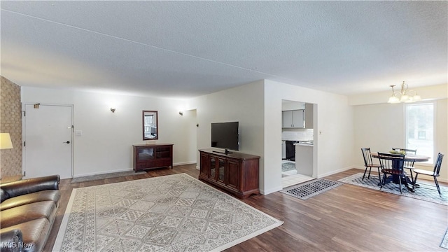 living room with a chandelier, dark wood finished floors, a textured ceiling, and baseboards