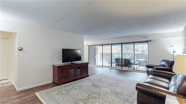 living room with visible vents, a textured ceiling, baseboards, and wood finished floors