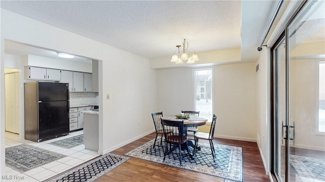 dining area featuring light wood-style floors, a chandelier, a textured ceiling, and baseboards