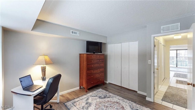 office area with a textured ceiling, wood finished floors, and visible vents