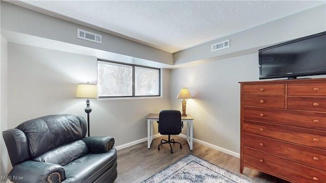 office space featuring light wood-type flooring, visible vents, a textured ceiling, and baseboards