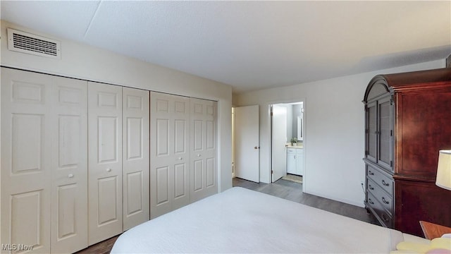 bedroom with ensuite bathroom, a closet, dark wood finished floors, and visible vents