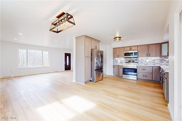 kitchen with stainless steel appliances, tasteful backsplash, light countertops, open floor plan, and light wood-type flooring